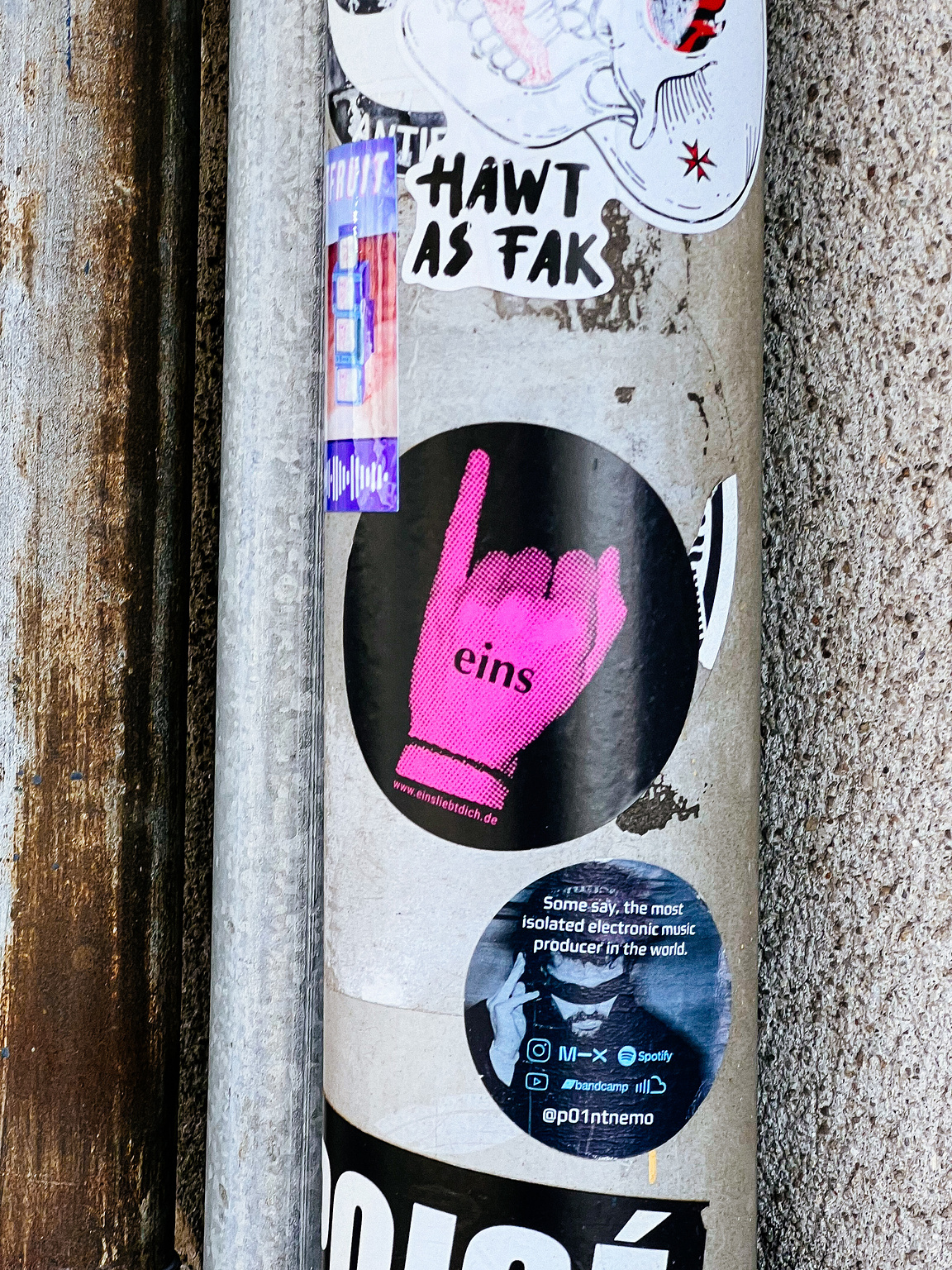 Various stickers are affixed to a pole, featuring graphics and text, including one with a pink hand and the word "eins."